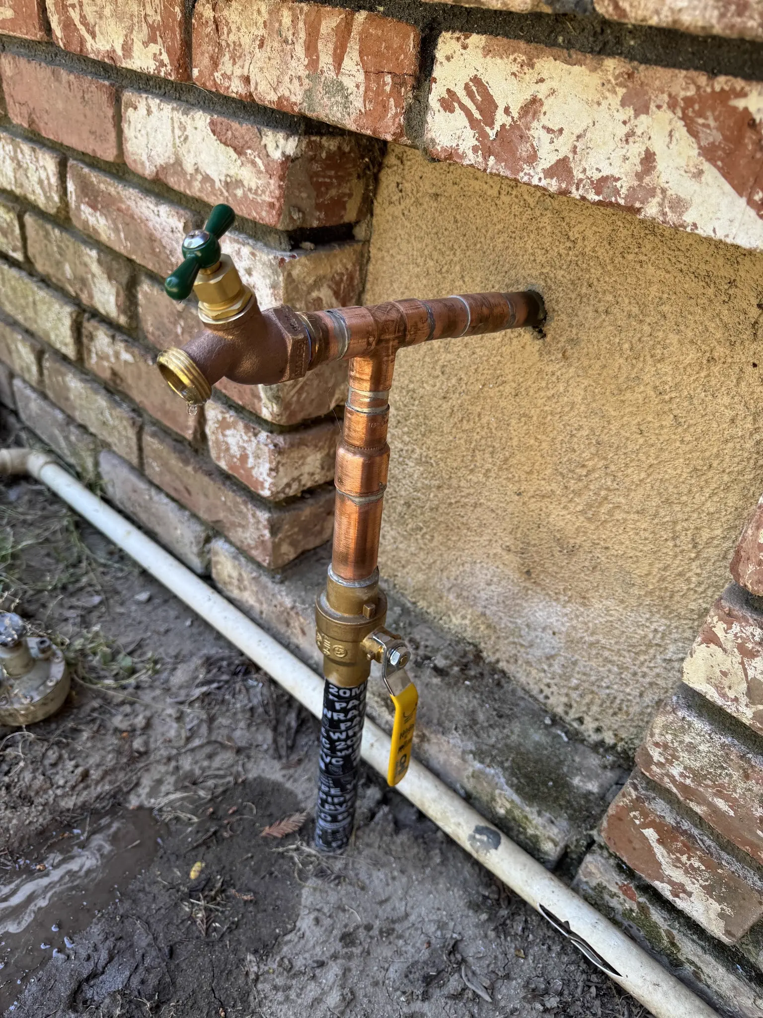 Accessible copper shutoff valve and outdoor spigot repair against a brick wall