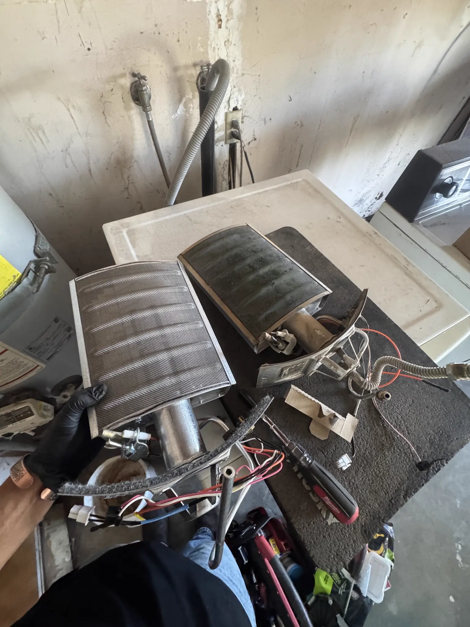 Old sooted water heater burner compared with a clean replacement burner during service